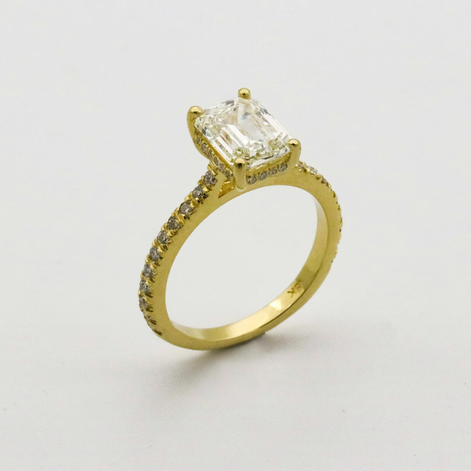 Close-up of an engagement ring with a rectangular centre stone on a pale background.