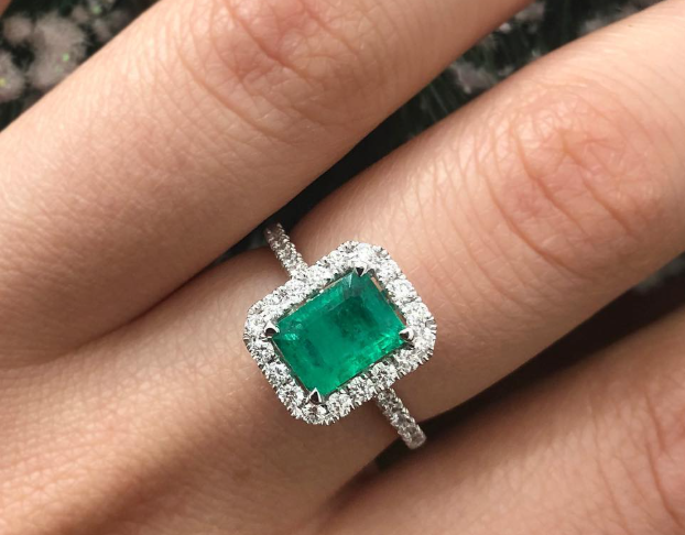 Rectangular green gemstone in a halo ring, shown on a hand.
