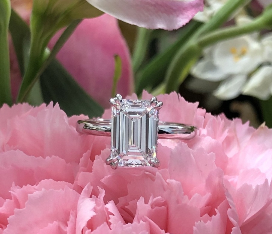 Emerald-cut solitaire ring resting on pink flowers.
