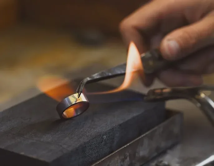 A torch flame playing over a wide band resting on a soldering block at the bench.