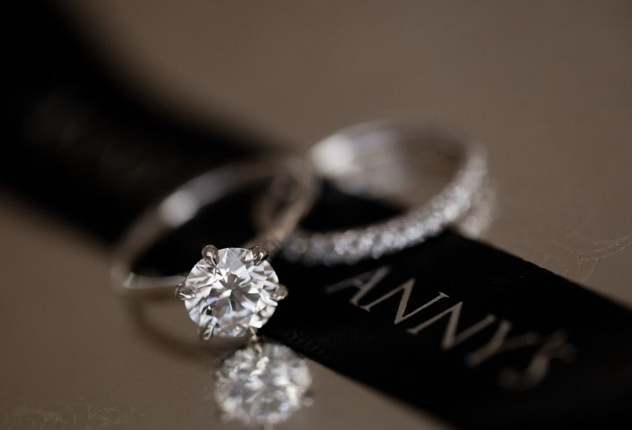 Round solitaire engagement ring beside a stone-set wedding band and a black Anny’s tag.
