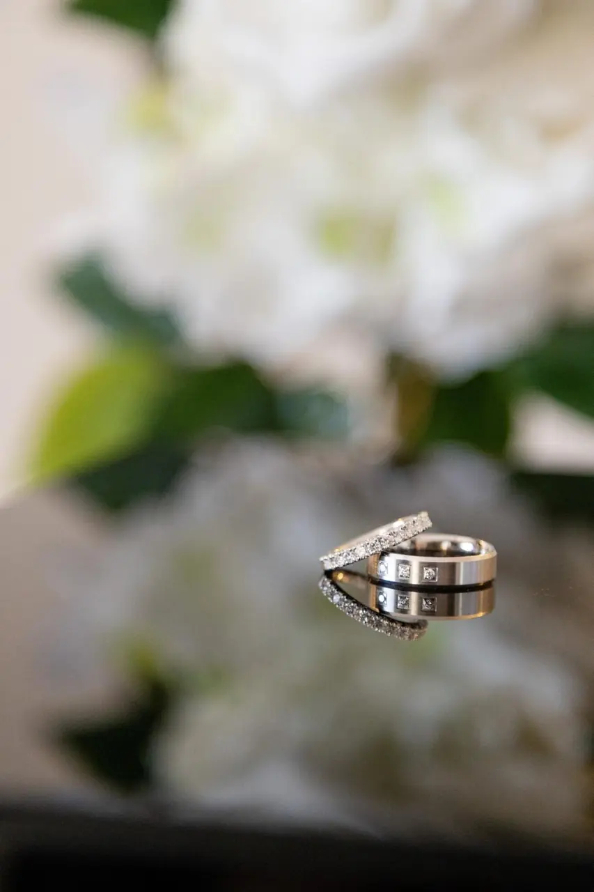 A brushed men's wedding band set with three small diamonds beside a diamond-set wedding band, reflected on a mirrored surface