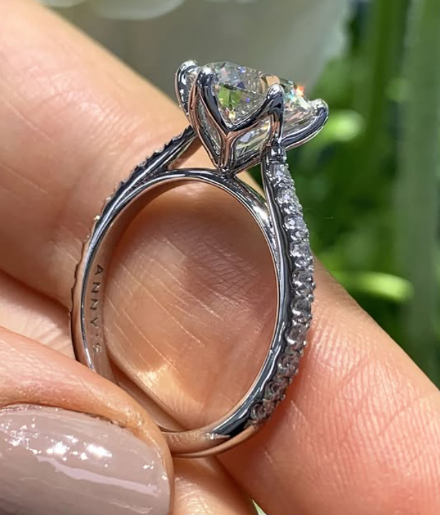 Finished 18ct white gold ring held between fingers, showing the white metal setting and the full circular band from the side.