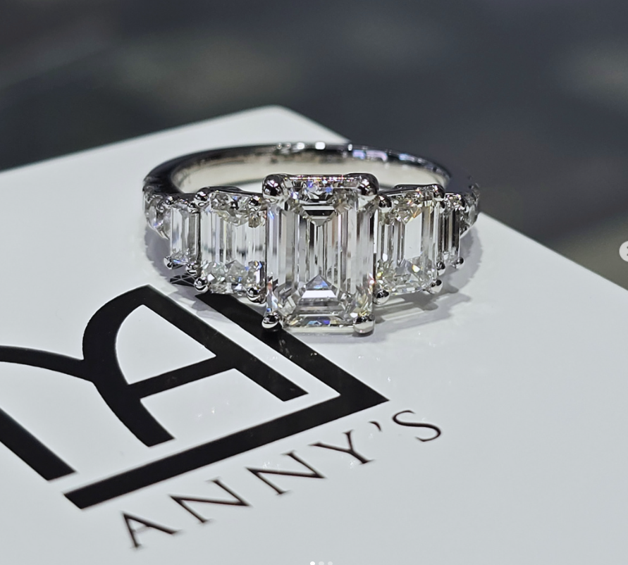 Platinum ring with a rectangular step-cut centre stone and graduated side stones on an Anny's display card.
