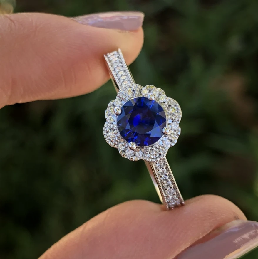 Blue-centred halo ring with a stone-set band, held between two fingers.