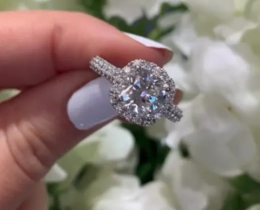 Cushion cut diamond ring held near white flowers