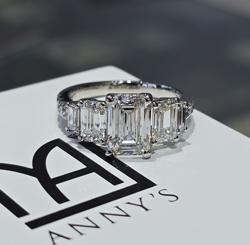 Emerald-cut natural diamond three-stone engagement ring with tapered emerald-cut side stones, in white metal.