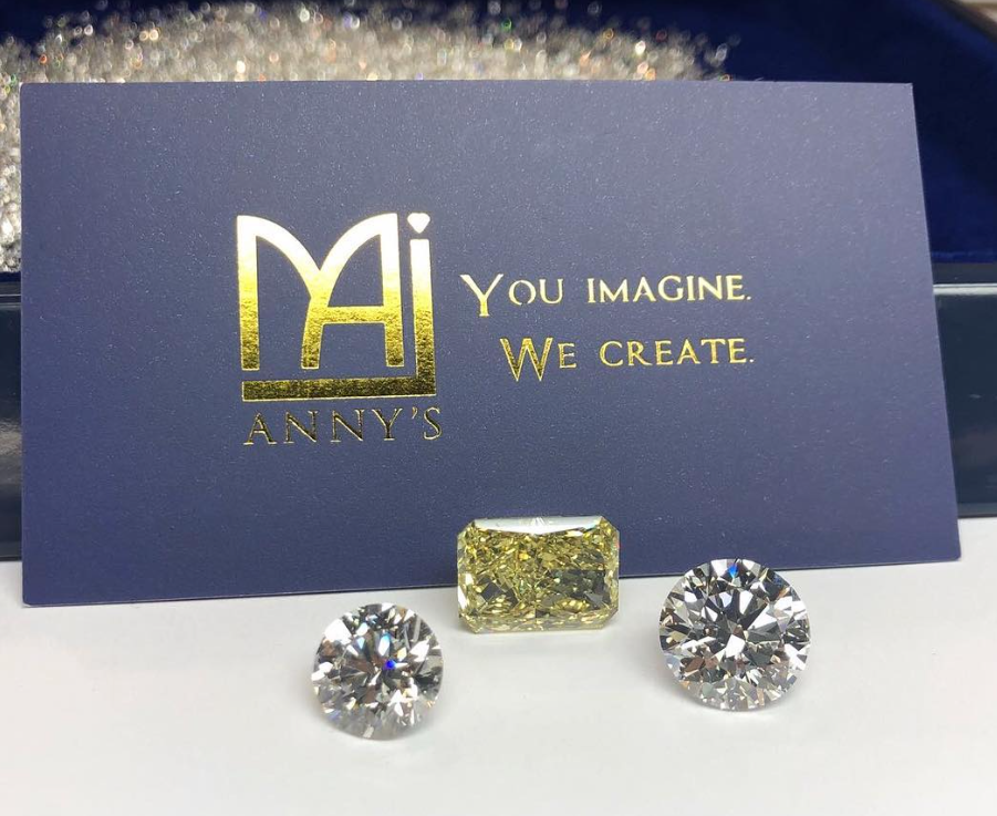 Two round brilliant natural diamonds and a fancy yellow radiant-cut diamond, loose in front of a navy Anny's card.