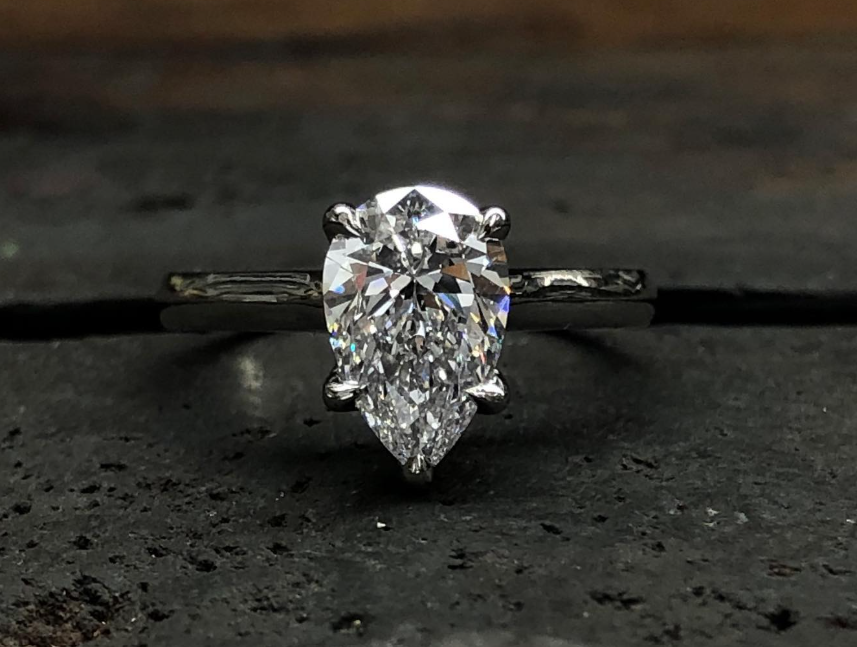 Pear-cut natural diamond solitaire in a five-claw white metal setting, photographed on a workshop bench.