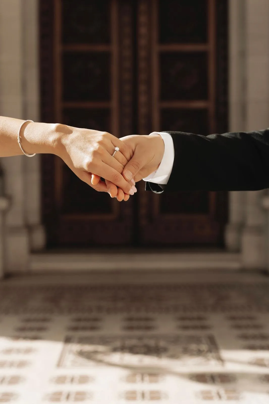 A couple holding hands, with a diamond engagement ring and wedding band