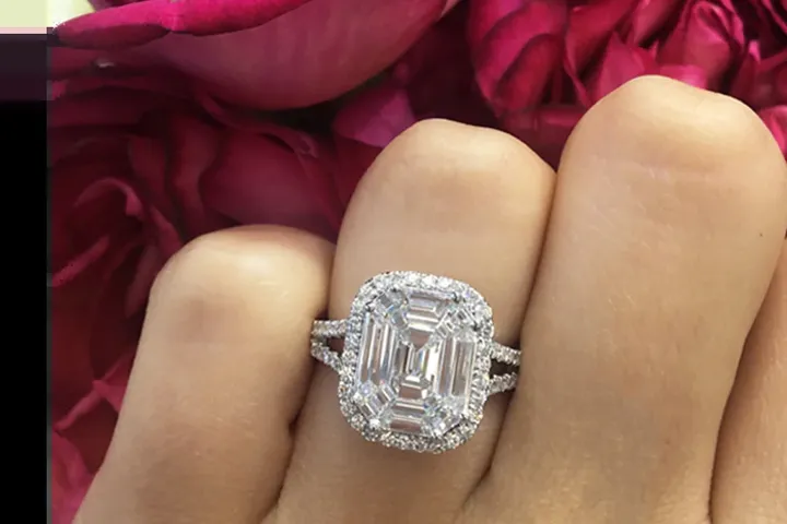 An emerald-cut halo diamond ring worn on a hand.