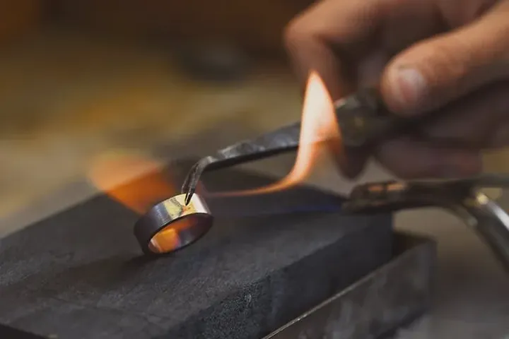 A jeweller soldering a ring band with a torch at the workbench.