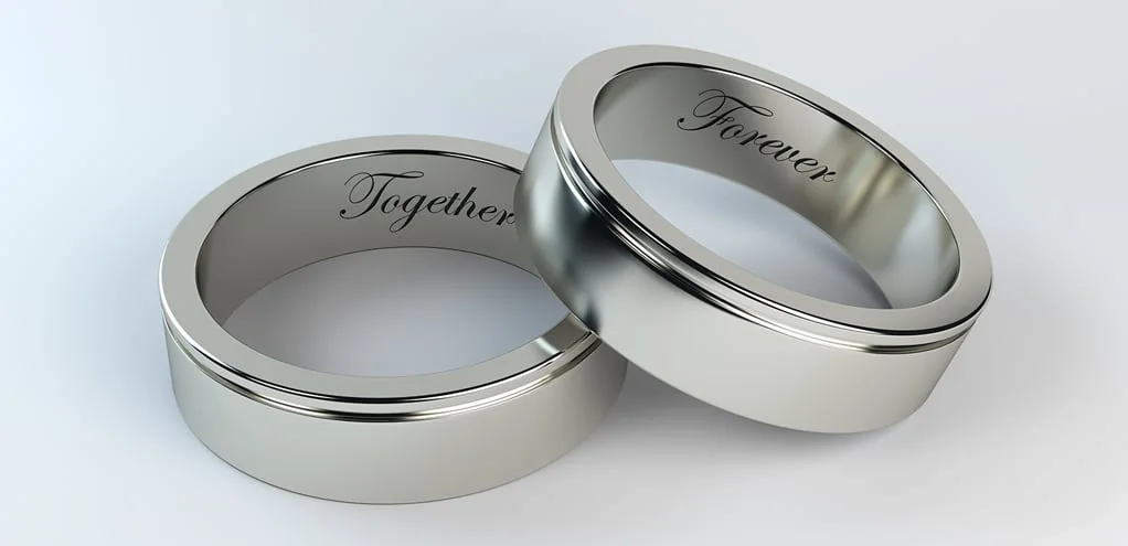 Two brushed white-metal wedding bands leaning together, engraved inside with the words Together and Forever.
