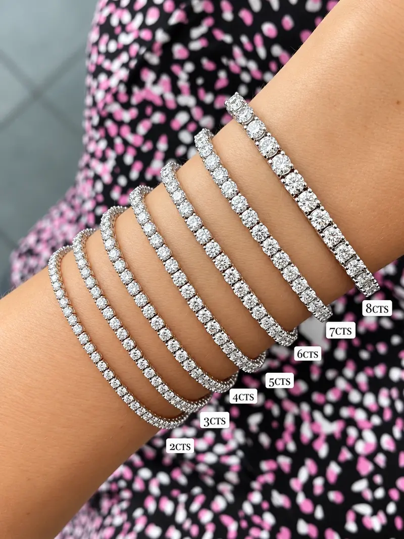 Seven white diamond tennis bracelets stacked on one wrist, from a fine 2 carat line to a bold 8 carat line, each labelled with its carat weight.